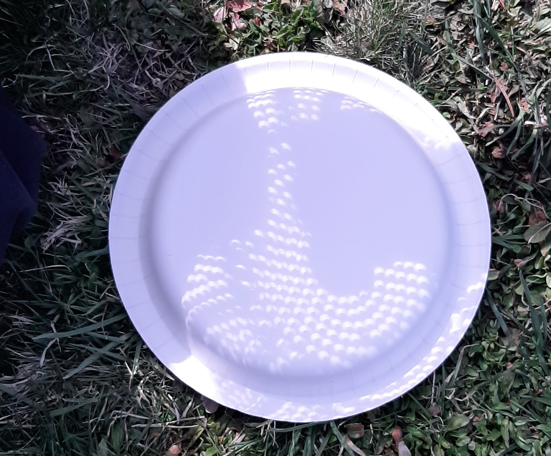 White plate with a colander held above it, showing the Moon's shadow.